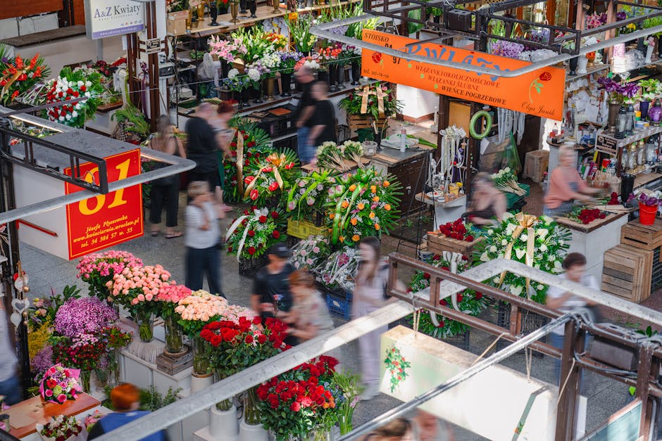 A bustling indoor flower market with numerous floral arrangements and bouquets on display, featuring a variety of fresh flowers such as pink, red, purple, and white roses, chrysanthemums, and lilies a