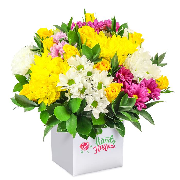 In this photograph, a lush, mixed bouquet spills generously over the top of a smooth white square gift box, the entire piece set against a white background that highlights the bright, contrasting tones. The flowers are arranged into a neat, rounded dome, tightly filled so that every angle appears abundant and considered, similar to the compact displays often seen in well-loved East Finchley cafés near Cherry Tree Wood. Deep golden yellow chrysanthemums and petite spray roses dominate the central area, their many overlapping petals giving a sense of plush softness and warmth, like captured afternoon sunshine. Interspersed among them are crisp white chrysanthemums and smaller daisy-style blossoms with vivid green centres, whose cool tones bring a refreshing clarity that balances the bouquet's richer hues. Vivid fuchsia and magenta chrysanthemums, some showing delicate gradations into lighter pinks, are artfully threaded throughout, providing accents of drama and feminine charm. The flowers are supported by a base of dark, glossy green foliage, leaves slightly curved and carefully placed to cradle the blooms and give the impression of freshly gathered garden stems. The white box acts as a minimalist vessel and presentation box in one, its clean lines emphasizing the playful softness of the petals above. The overall effect is that of a joyful, approachable bouquet-elegant yet affordable-well suited to birthdays, get-well wishes, or simply brightening a kitchen table or office in East Finchley. It feels like a thoughtful, same-day gift that brings a little burst of local colour and happiness indoors, whether for family, friends, or colleagues.