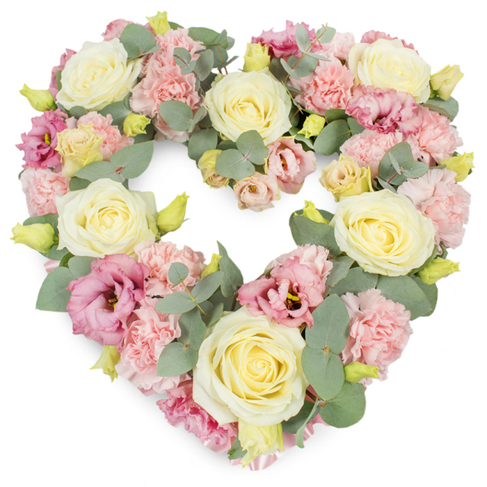 The photograph shows a meticulously crafted heart-shaped wreath, overflowing with soft, pastel blooms and framed by cool-toned greenery, all set against a pristine white background. Cream and pale yellow roses are the stars of the arrangement, each rose fully open yet still neat, their spiralling petals forming rounded cups of light that punctuate the heart. Between and around them, a profusion of pale pink carnations creates a rich, velvety texture, every frilled petal overlapping the next to give a sense of depth and abundance. Deeper rose-pink and mauve lisianthus flowers are interspersed with a florist's eye for balance, their slightly looser, more papery petals and darker centres drawing the gaze inward and adding emotional resonance. Woven throughout are slender stems of eucalyptus, their silvery-green, almost blue-grey leaves hugging the curves of the design and providing a gentle, herbal freshness in the imagination. Tiny buds in yellow-green are scattered like quiet notes of new life, hinting that even in moments of farewell, growth and love continue. The heart shape is clear and symmetrical, with no gaps, conveying a sense of completeness and unwavering devotion. It is the sort of funeral tribute that might be chosen for a service in East Finchley, perhaps travelling from the local high street florist to a ceremony at a nearby church or crematorium. The gentle colour palette and lush composition make this wreath a comforting, dignified expression of sympathy and remembrance, suitable for honouring a parent, partner, or close friend with warmth and grace.