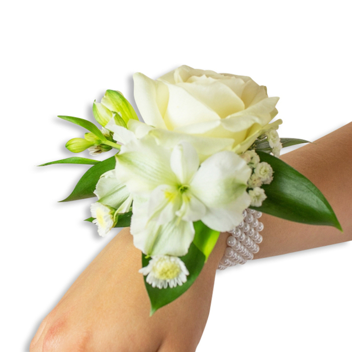 A refined white wrist corsage photographed from a gently elevated angle against a clean, untextured white background, where every shape and shade reads clearly. The composition is centred by a plush, creamy ivory rose, its petals forming concentric, velvety layers that reflect a soft, diffuse light and create a sense of quiet luxury. Slightly below and left, a trumpet-shaped alstroemeria-like bloom reveals a subtle lime-green throat, the delicate ribbing of its petals adding dimensionality and a whisper of colour beneath the dominant whites. Interspersed throughout are fresh green buds-small, taut and hopeful-paired with airy clusters of gypsophila that float between larger blooms like soft breath. Toward the lower left a small grouping of daisy-like white florets with sunny yellow centres contributes a touch of playful innocence to the otherwise elegant piece. Generous, glossy deep green leaves with smooth surfaces cradle the flowers, their saturated tone providing a lush backdrop that makes the whites sing. The arrangement is anchored to the wrist by an elegant, elastic multi-strand pearl band; the beads are uniformly round and luminous, offering a tactile, classic counterpoint to the living flowers. There is an almost imperceptible scent-clean rose and fresh cut stems-that evokes early morning deliveries from the market. This corsage reads as timeless and carefully made, a perfect accent for weddings, formal dances, or a meaningful evening out in East Finchley near Market Place and the local High Road.
