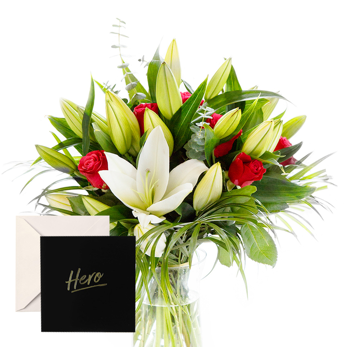 As a local florist, I know that blending boldness with serenity can create something both striking and comforting. This arrangement places white lilies at its heart, their large, trumpet-shaped blooms catching the eye with a soft, satin sheen. They are surrounded by vibrant red roses, each bloom a symbol of love and respect, while a cascade of green foliage-dense, glossy leaves with a touch of forest texture-threads through the bouquet. Unopened lily buds punctuate the composition, hinting at future beauty and new beginnings, all set in a softly lit, natural moment that feels close to the heart.
The light here is gentle, turning the whites to pearl and the reds to velvet, lifting the whole piece into an effortless, uplifting mood. The arrangement feels alive as if it were a living garden gathered from the edge of Cherry Tree Wood and placed in a clear vase, inviting the eye to move with its rhythm. It is designed to honour someone's strength or achievement with grace, a refined tribute that remains warm and personal, never overpowering.
An accompanying card marked Hero seals the gesture, making this more than a display of beauty-it's a story of admiration and encouragement. In East Finchley, this bouquet finds its way to desks, event stages, or doors, a flexible companion for thank-yous, congratulations, or shared pride.
Delivered across East Finchley and nearby streets, this bouquet is a testament to local craft: balanced, enduring, and ready to accompany a moment of significance with fresh stems and lasting fragrance.
