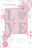 In this photograph, a romantic anniversary card is displayed, its artwork radiating the same subtle charm as a hand-tied bouquet delivered across East Finchley. At the centre, the word LOVE appears in substantial, raised capital letters, richly textured with a fine layer of pearlescent white and blush-pink glitter. This sparkling finish is delicate, catching the light in a soft gleam that suggests candlelight glancing off flower petals rather than a harsh shine. The letters rest against a smooth, pastel-pink background, gently shaded to give the impression of depth and warmth, like the inner folds of a rose. Encircling the central word, slender stems, stylised blooms, and small leaves spread across the card in sweeping curves. These floral elements are illustrated with light grey lines and subtle silver accents, evoking the loose, flowing layout a local florist might sketch when planning an anniversary arrangement for a home near Cherry Tree Wood or along East End Road. The blossoms vary in size, yet all remain airy and refined, their shading soft and understated, creating a sense of motion as if the flowers were gently nodding in a breeze. The photograph is lit with a gentle, diffuse light that reveals the contrast between the matte card, shimmering glitter, and metallic ink, giving the design a layered, tactile feel. Elegant script text, written in a graceful, cursive-style font, conveys heartfelt anniversary wishes and a message of lasting devotion. The overall mood is tender, elegant, and timeless, echoing the feeling of celebrating another year together with fresh flowers and quiet moments at home in East Finchley.